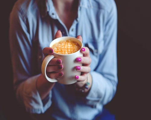 A person holding a warm cup of coffee looking out the window
